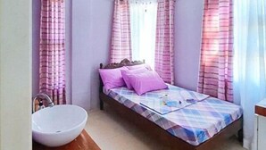 A single bed with a checkered bedspread, two pillows, a wooden headboard, and a white sink in a bathroom with pink curtains. - Bahai Jujai Baler by RedDoorz (Baler)