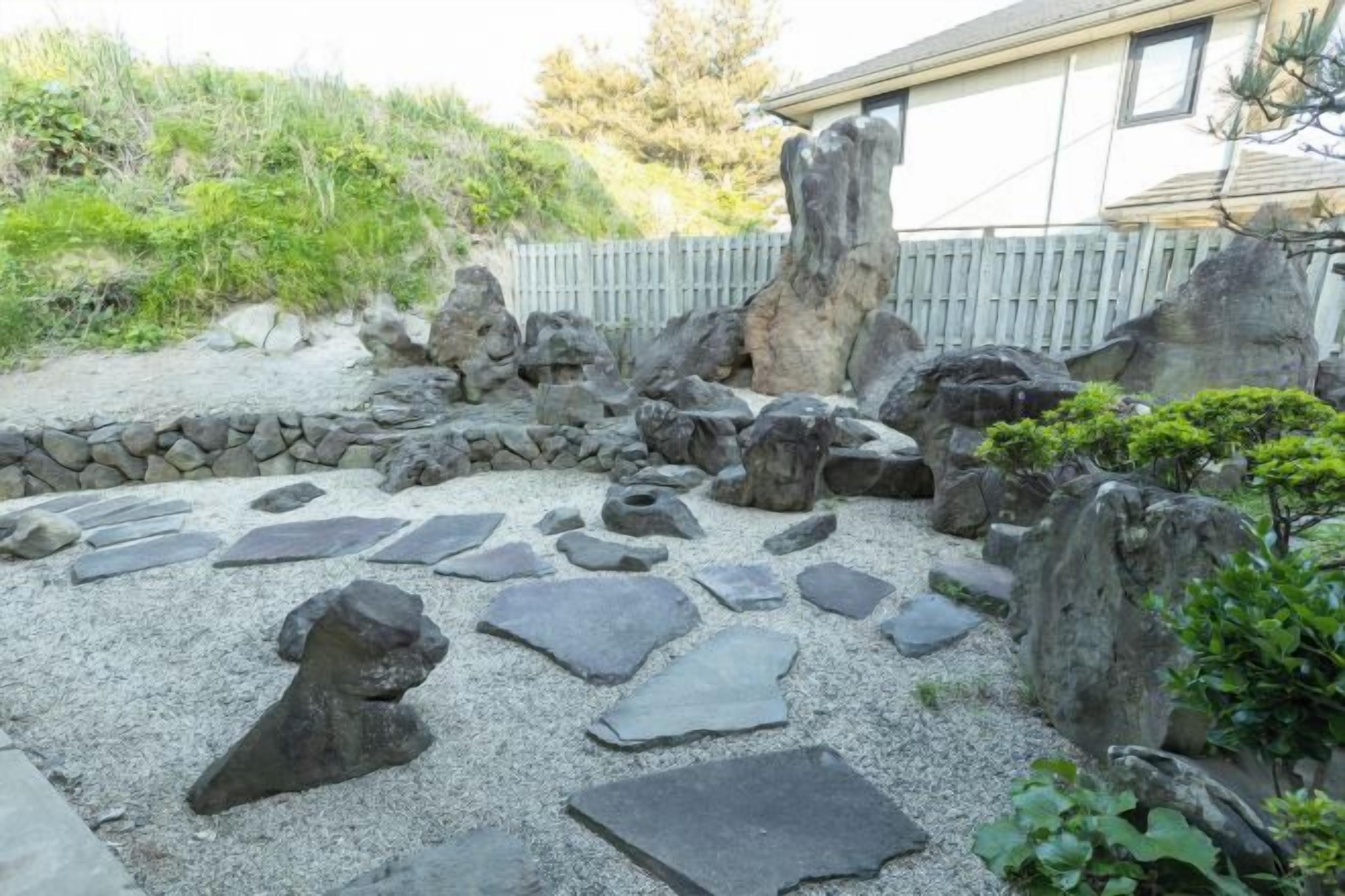 A garden with a stone pathway, rocks, and a wooden fence.