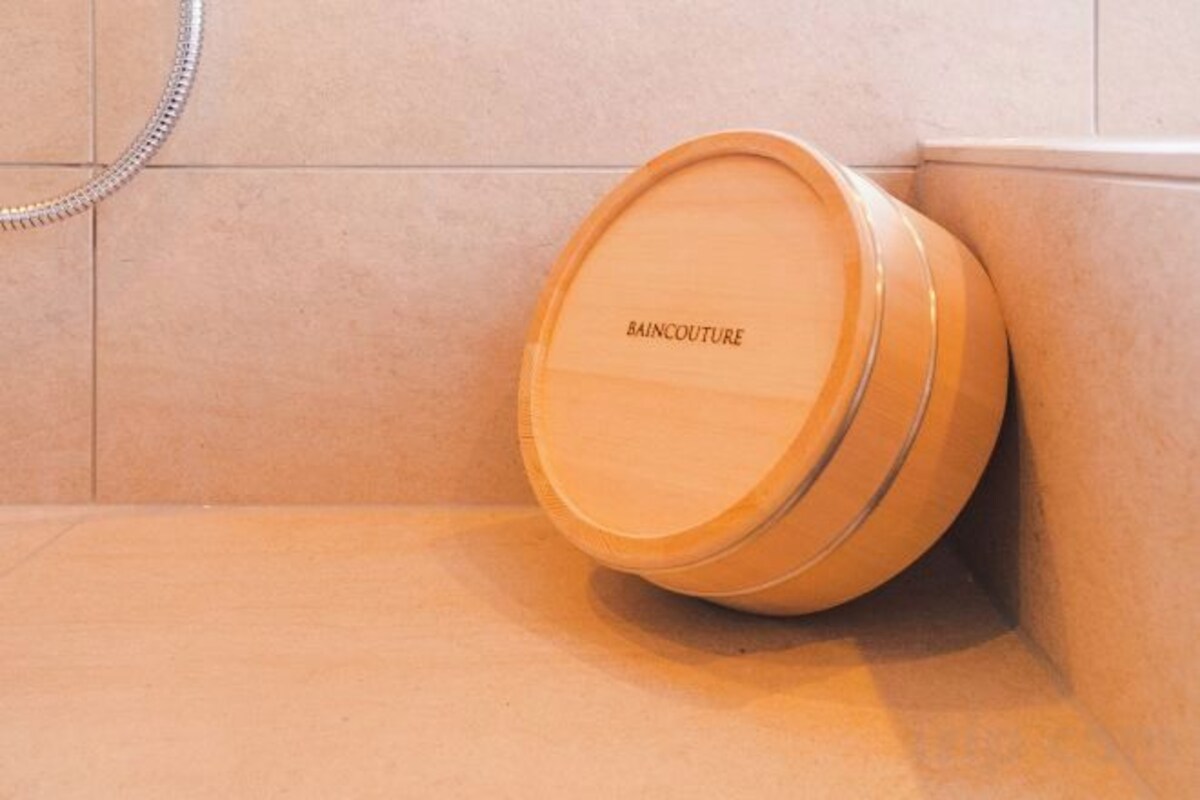 A bathroom with a shower area, a bathtub, and a wooden container labeled 'BAINCOUTURE' on the floor.