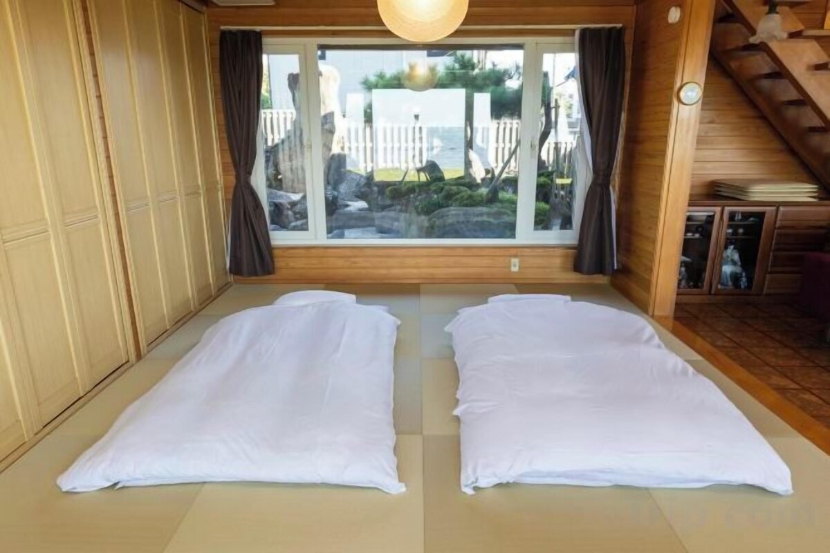 Ein Zimmer mit Tatami-Matten, einer Schiebetür mit Blick und einer Holzbalkendecke.