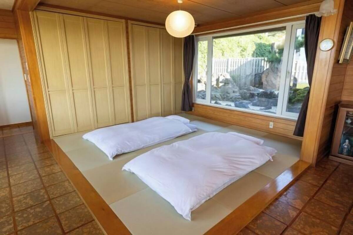 Ein Zimmer mit einem Bett, einem Fenster mit Blick auf Felsen und Grünflächen, und einer Holzziel.