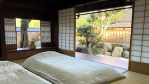 A traditional Japanese room with tatami flooring, a low wooden bed, and a view of a garden through shoji screens.