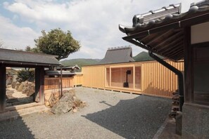 A traditional Japanese building with a wooden exterior, a gravel courtyard, and a large tree. - tehen -roots stay- (Kyoto)