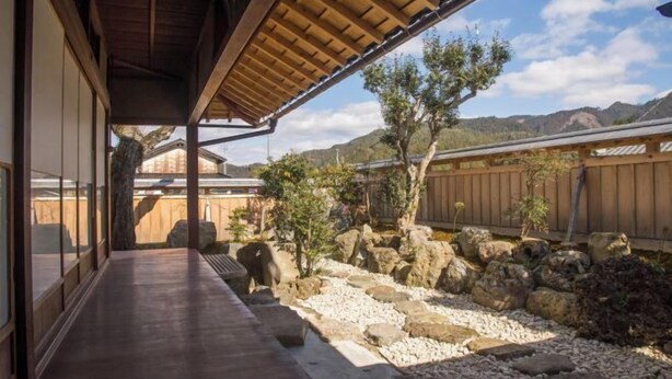 A traditional Japanese-style building with a wooden deck and a view of a landscaped garden with rocks and a tree.