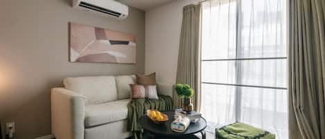 A living room with a sofa, a round coffee table, and a window with curtains.