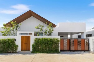 A modern two-story house with a wooden door, white walls, and a brown roof.
