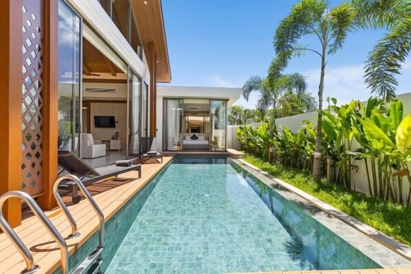 A modern pool area with a clear pool, wooden deck, and lounge chairs.