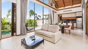 A spacious living area with a large window overlooking a pool, a modern kitchen, and a cozy seating area. - The Ozon Bangtao 3-bedrooms Villas with pool by My Home Phuket (Phuket)