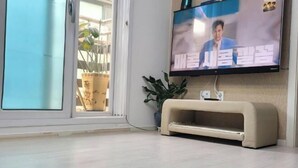 A living room with a television mounted on the wall, a beige sofa, and a potted plant. - jeni's house (Seoul)
