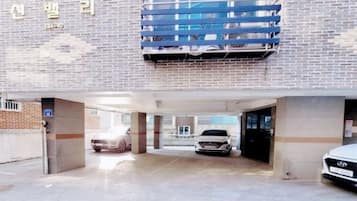 Entrada de estacionamento com fachada de tijolos, toldo azul e um carro branco estacionado lá dentro.