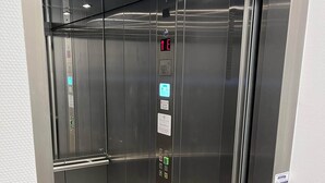 Un ascensor moderno con pantallas digitales, botones de emergencia y pasamanos.