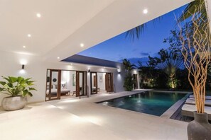 Een modern huis met een zwembad, glazen deuren naar een terras en uitzicht op de lucht.