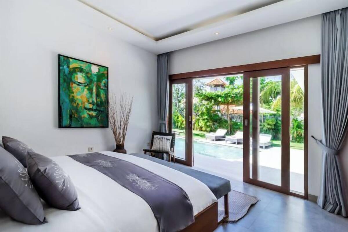 Ein Schlafzimmer mit einem Bett, einem Gemälde, einem Sessel und Blick auf einen Swimmingpool.