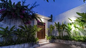 A modern house with a wooden door, a brick pathway, and lush greenery.