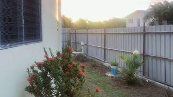 A fenced backyard with a small garden area, a wooden fence, and a house with a window.