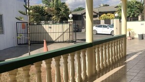 A covered outdoor area with a tiled floor, a metal gate, and a white car parked in the background. - Ac airport apartment (Nadi)