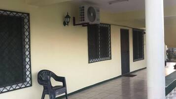 A corridor with tiled flooring, a black plastic chair, and air conditioning units mounted on the wall.