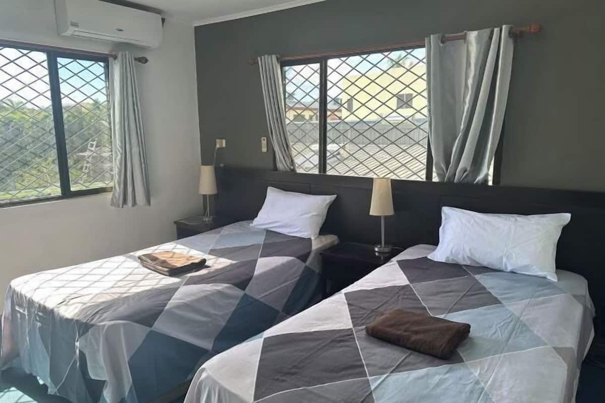 A hotel room with two beds, each with a patterned bedspread, a nightstand with a lamp, and a window with curtains.