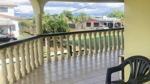 A balcony with a tiled floor and a chair, overlooking a residential area with houses and greenery. - Ac airport apartment (Nadi)