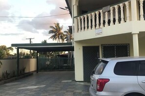 Een gebouw met een overdekte ingang, een auto ervoor en een balkon met hekwerk.