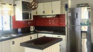 A kitchen with white cabinets, a red backsplash, a stainless steel refrigerator, and a microwave. - Ac airport apartment (Nadi)