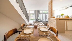 A dining area with a long table set for four, a kitchen area with a stone backsplash, and a staircase leading to an upper floor. - Villa Casa Antonio (Bali)