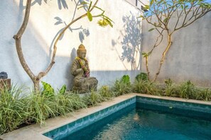 A statue of a deity by a pool with a concrete wall and greenery. - Villa Casa Antonio (Bali)