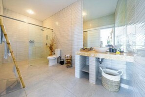 A modern bathroom with a glass shower enclosure, a toilet, and a vanity with a sink and mirror. - Villa Casa Antonio (Bali)