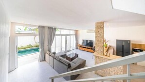 A modern living room with a large TV, a stone pillar, and a pool view. - Villa Casa Antonio (Bali)
