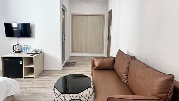 Ein Hotelzimmer mit braunem Ledersofa, einem schwarzen Couchtisch, einem an der Wand befestigten Fernseher, einem Holzschrank und einem kleinen Schreibtisch mit Wasserkocher und Flaschen.