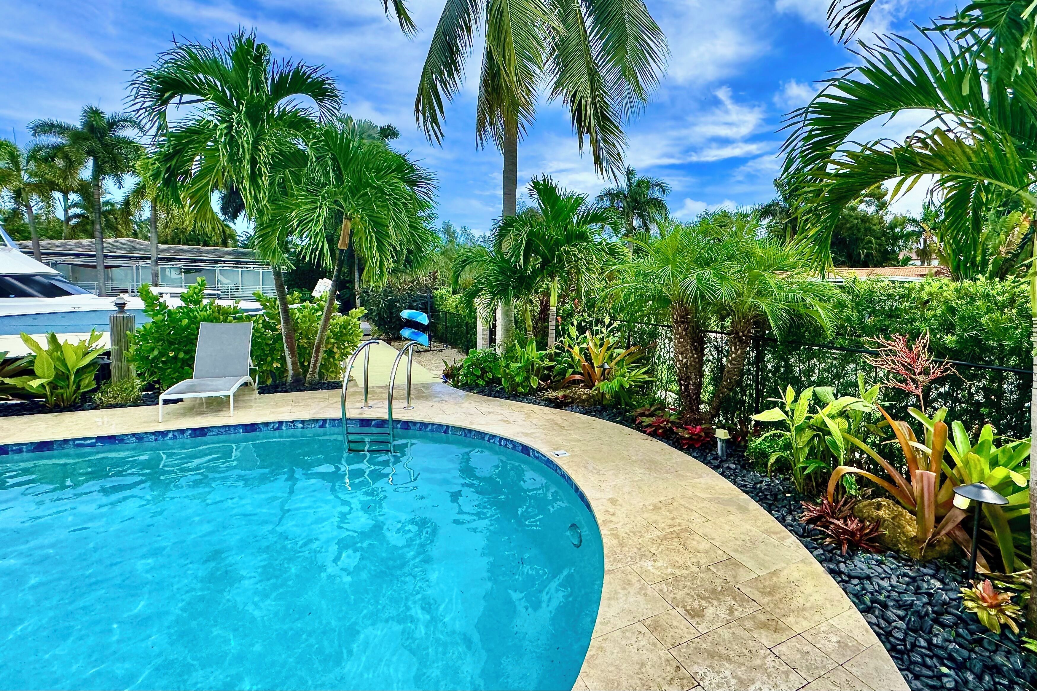 A swimming pool with lounge chairs, surrounded by tropical plants and palm trees.