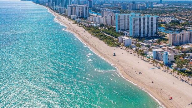 A coastal cityscape with a beach, high-rise buildings, and clear blue waters.