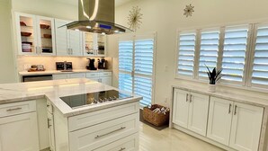 A modern kitchen with white cabinetry, a central island with a stovetop, and a window with blinds.