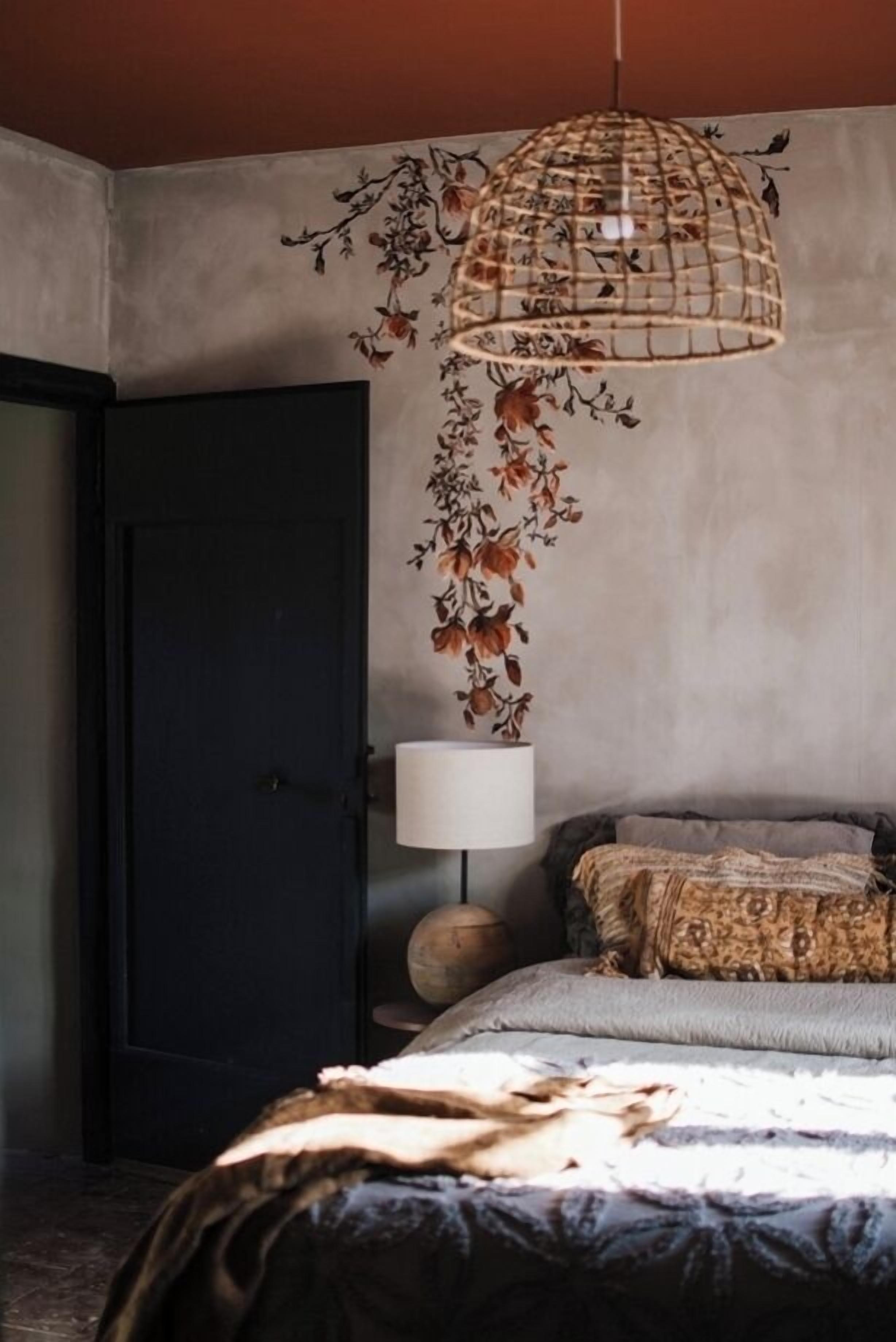 A bedroom with a bed, a hanging light fixture, a door, and a wall with a floral pattern.