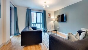 A modern living room with a sofa, a coffee table, and a TV mounted on the wall. - Sage Apartments - by Week2Week (Gateshead)