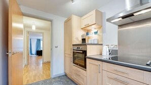 A modern kitchen with wooden cabinets, a stainless steel range hood, and a tiled floor. - Sage Apartments - by Week2Week (Gateshead)