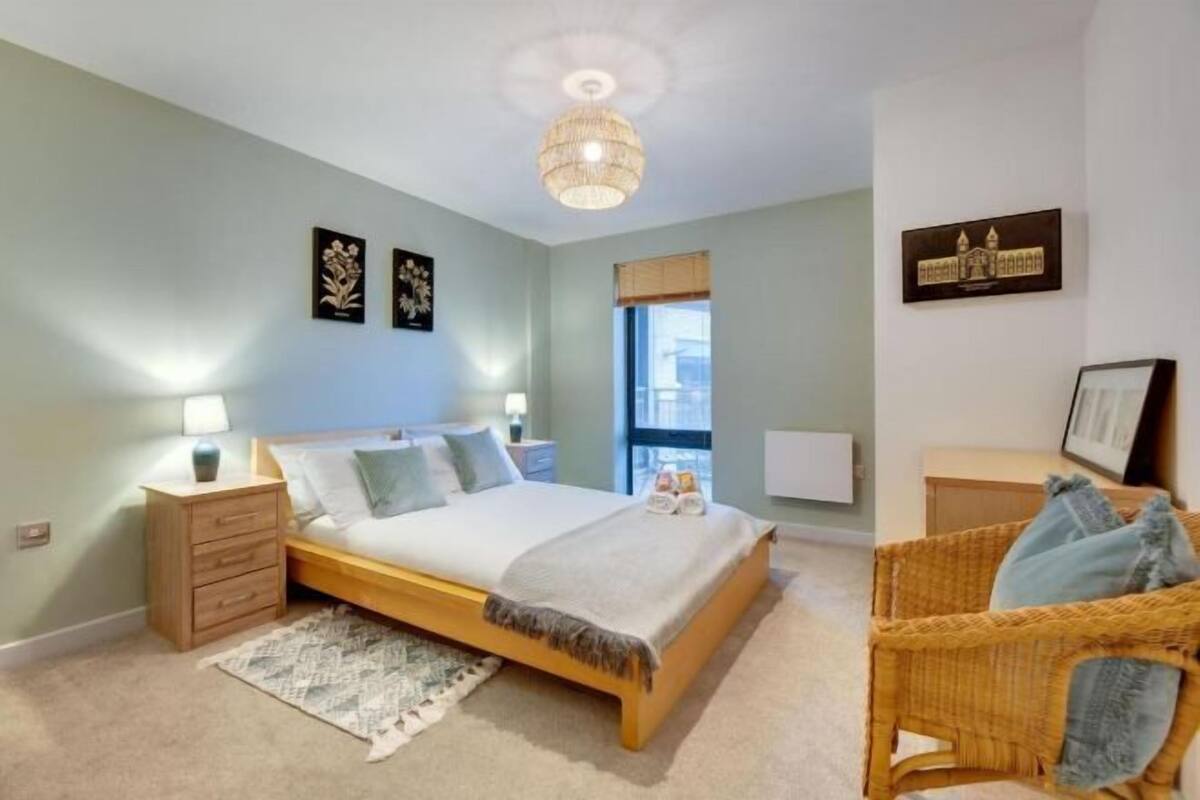 A bedroom with a bed, bedside tables, a wicker chair, and wall art.