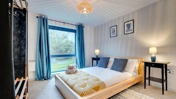 A bedroom with a bed, bedside tables, a window with curtains, and a ceiling light fixture. - Sage Apartments - by Week2Week (Gateshead)
