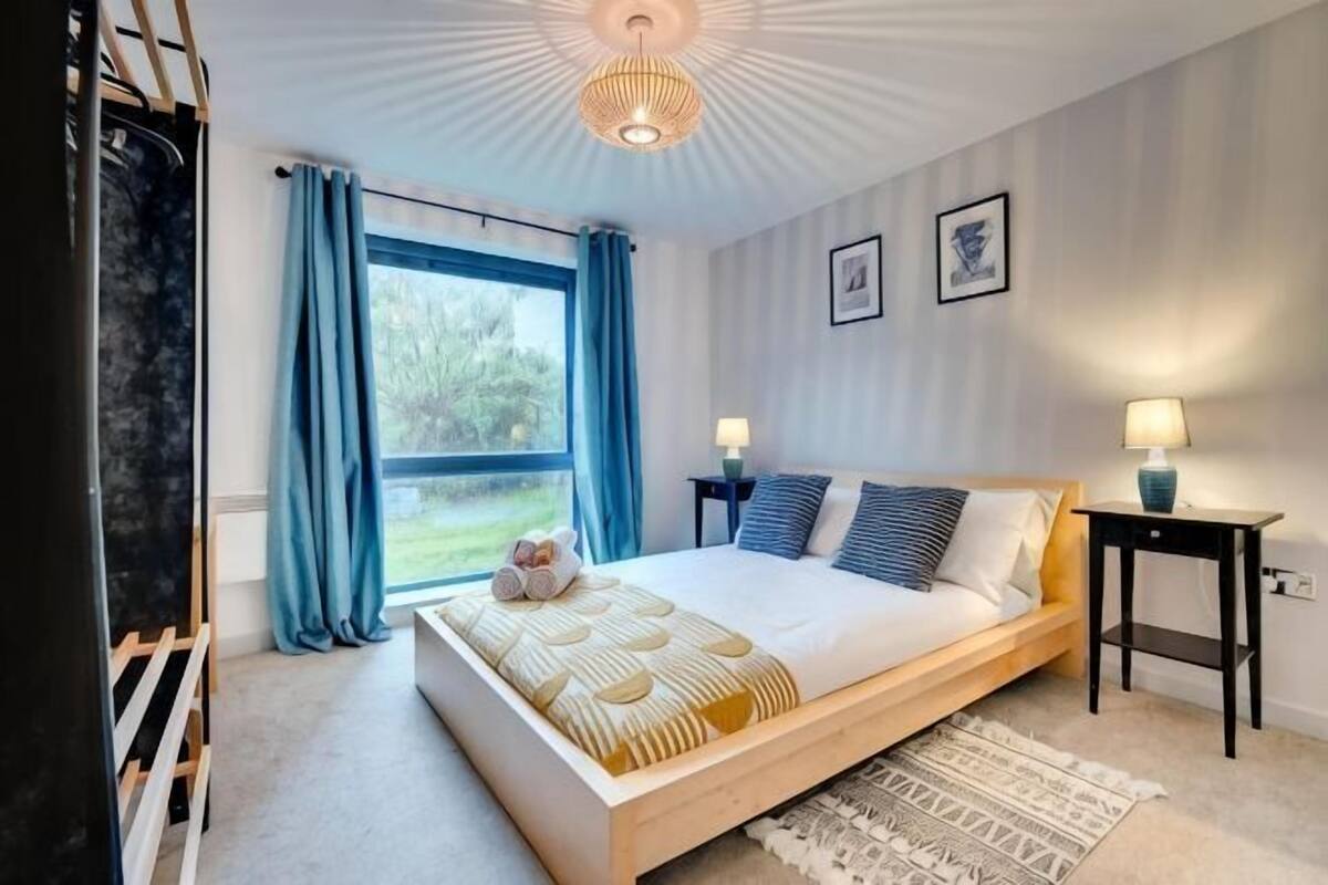 A bedroom with a bed, bedside tables, a window with curtains, and a ceiling light fixture.