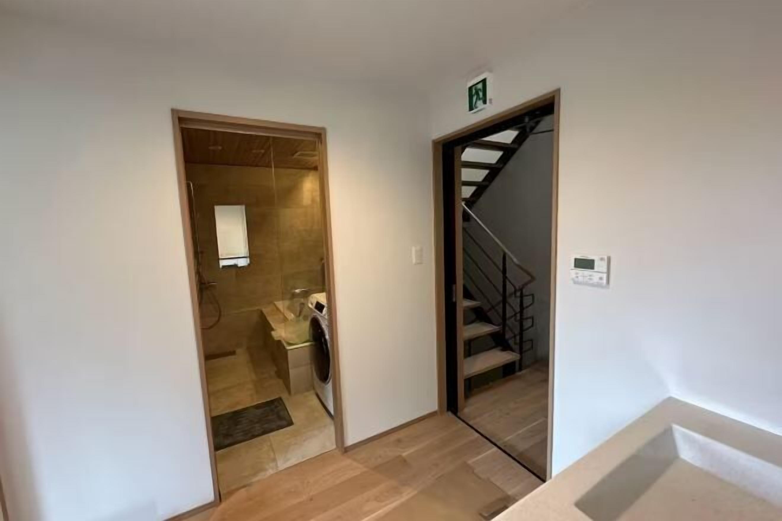 Um corredor com máquina de lavar, escada e porta que dá para outro quarto.