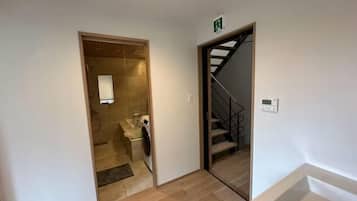 Um corredor com máquina de lavar, escada e porta que dá para outro quarto.