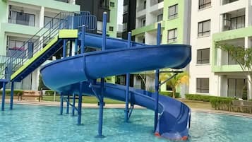 A blue water slide in a swimming pool area with multi-story buildings in the background.