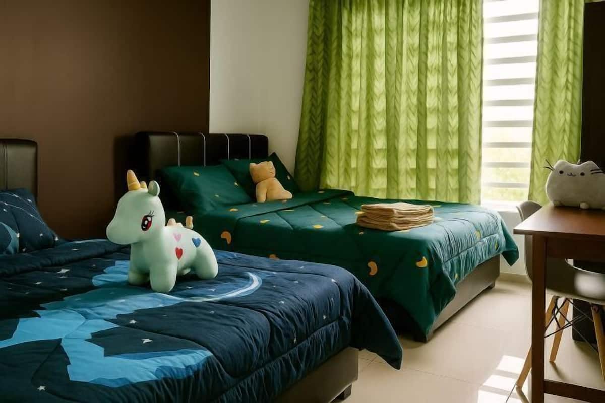 Ein Hotelzimmer mit zwei Betten, einem Schreibtisch und einem Fenster mit grünen Vorhängen.