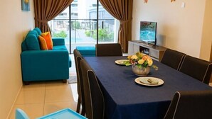 Een zithoek met een tafel voor twee personen, een bank en een televisie op de achtergrond.