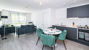 Una cocina moderna con armarios oscuros, una encimera blanca y un comedor con una mesa redonda y sillas verdes.