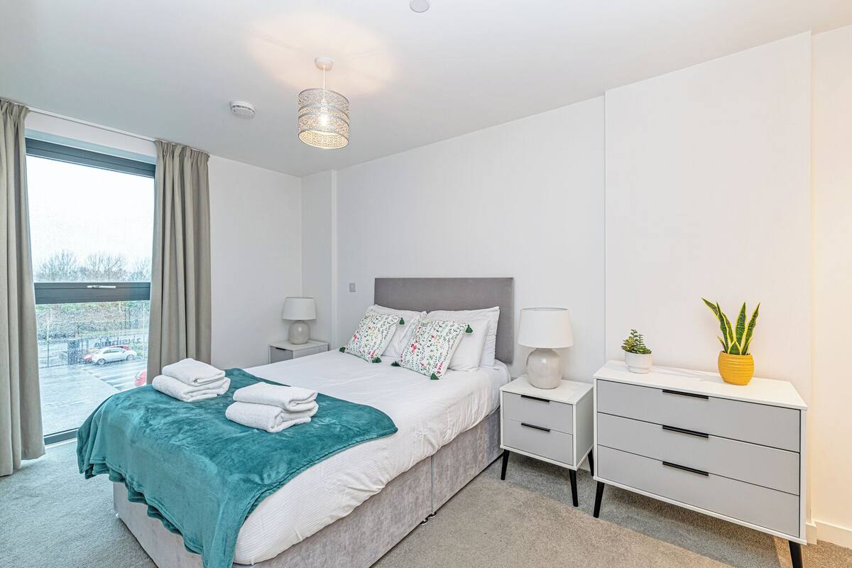 A modern bedroom with a bed, bedside tables, a lamp, a potted plant, and a view of the outside.