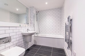 Un baño moderno con azulejos blancos tipo metro, un lavamanos blanco, una bañera y un inodoro.