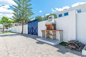 An outdoor barbecue area with a grill, a blue gate, and a white wall. - Villa Lucentum (Alicante)