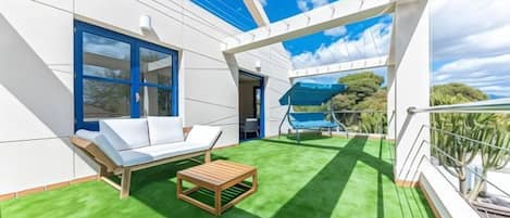 Un balcón con un sofá blanco, una mesa de madera y vistas al mar.