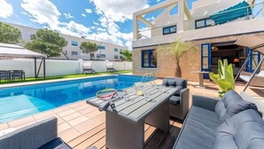 A pool area with a table and chairs, a lounge chair, and a building with a balcony. - Villa Lucentum (Alicante)